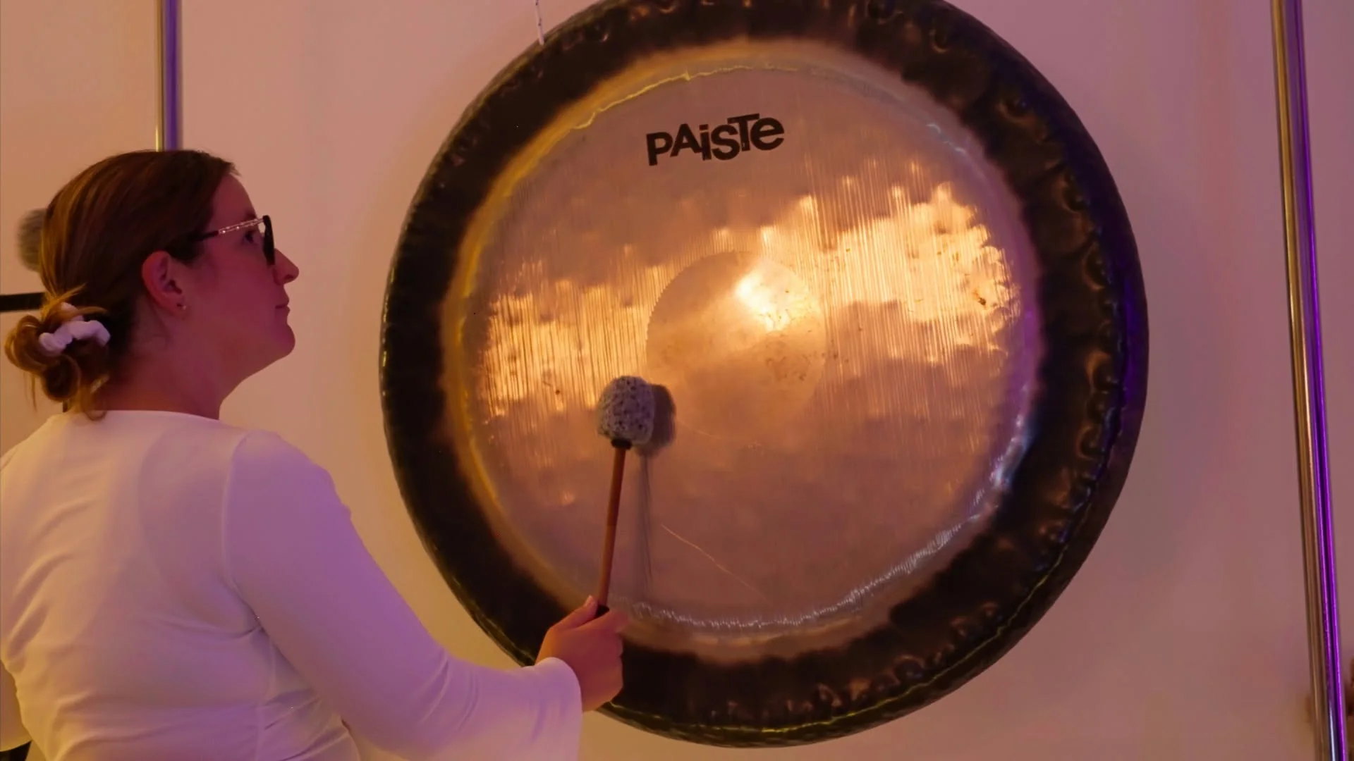Maillet tenu devant un grand gong aux reflets dorés et violets.